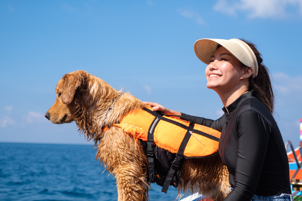 A young woman and a golden retriever dog with life jacket sitting on a boat while sailing in the sea